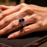 Gros plan d’une main portant une bague en saphir bleu profond dans un écrin de bijouterie élégant, avec une lumière douce et une ambiance raffinée.