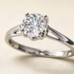Gros plan d’une bague de haute joaillerie en or blanc ornée d’un diamant suspendu, éclairée par une lumière douce sur fond clair.